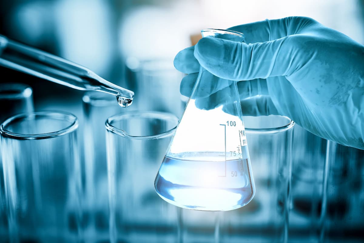 A blue-gloved scientist holding a beaker and an eyedropper